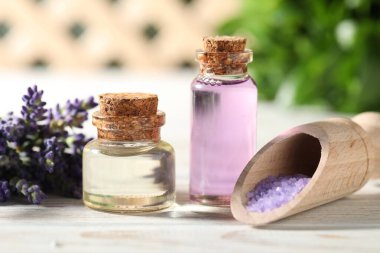 Beyaz ahşap masa üzerinde gerekli yağ, çiçek ve deniz tuzu şişeleri, yakın plan.