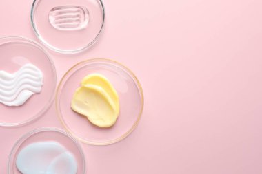 Petri kaplarında pembe arka planda farklı kozmetik ürünleri var. Metin için boşluk