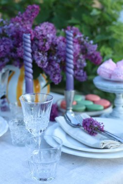 Güzel leylak çiçekleri, tatlılar, tabaklar, çatal bıçak takımı, bardaklar ve mumlar bahçede, yakın plan