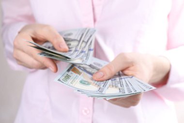 Açık gri arka planda dolar banknotları sayan kadın, yakın plan