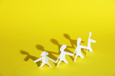 Sarı arka planda el ele tutuşan insan kağıt figürleri. Metin için boşluk