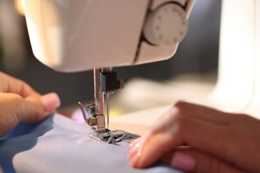 Bulanık gri arkaplan ve makro görünüm üzerinde dikiş makinesiyle çalışan kadın