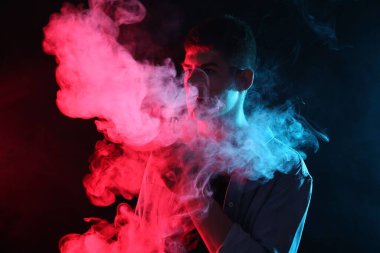 Koyu arkaplandaki neon ışıklarda elektronik sigara içen adam