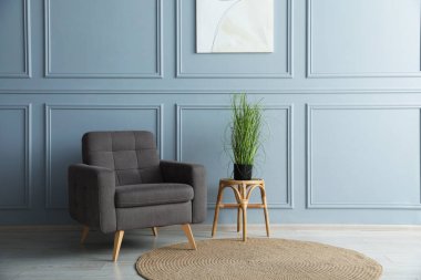 Açık mavi duvarın yanında rahat bir koltuk ve ev bitkisi.