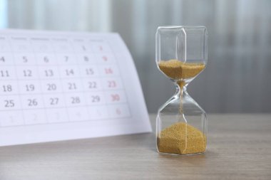 Son teslim tarihi. Kapalı alanda ahşap masada kum ve takvim akan kum saati.