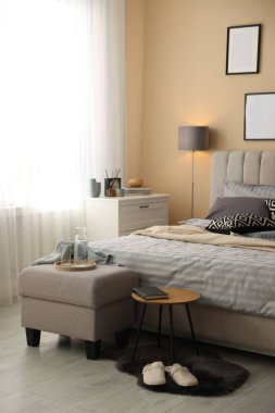 Yumuşak çarşafları, terlikleri, puf ve yan masası olan rahat bir yatak. Ev tekstili