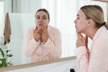 Banyoda aynanın yanında sivilce çıkaran bir kadın. Sivilce sorunu