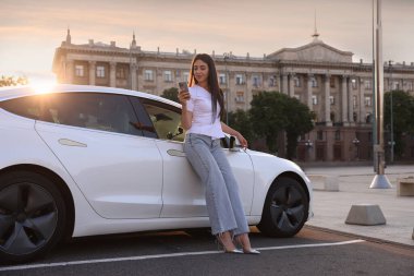 Güneşli bir günde modern arabanın yanında akıllı telefonu olan güzel bir kadın.