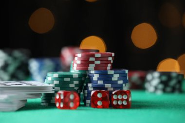 Kumarhane fişleri, zarlar ve iskambil kartları yeşil masada bulanık ışıklara karşı, yakın plan