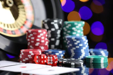 Kumarhane fişleri, iskambil kartları, rulet tekerleği ve zarlar ayna yüzeyinde bulanık ışıklara karşı, yakın plan