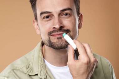 Yakışıklı bir adam açık kahverengi arka planda dudaklarına merhem sürüyor.