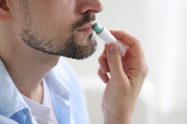 Bulanık ışık arka planında dudaklarına dudak kremi süren bir adam.