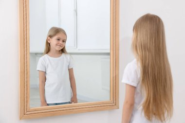 Güzel küçük kız aynada kendine bakıyor.