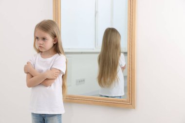 Evdeki aynanın yanındaki üzgün küçük kız.