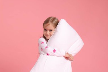 Pembe arka planda yastıklı pijamalı şirin bir kız.