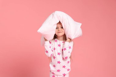 Pembe arka planda yastıklı pijamalı şirin bir kız.