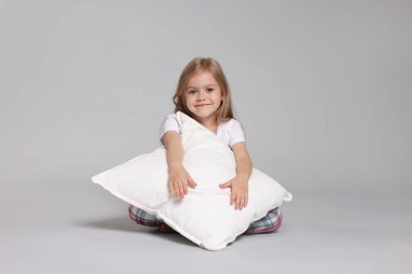 Gri arka planda yastıklı pijamalı şirin bir kız.