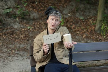 İşaretli evsiz adam Yardım ve kağıt bardak Parktaki bankta para dileniyor