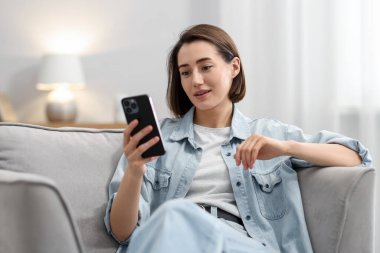 Evdeki koltukta modern akıllı telefon kullanan bir kadın.