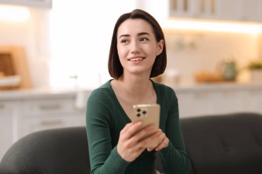 Evdeki koltukta modern akıllı telefon kullanan bir kadın.