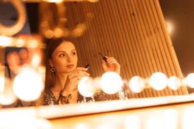 İçeride aynanın yanında maskara süren güzel bir kadın.