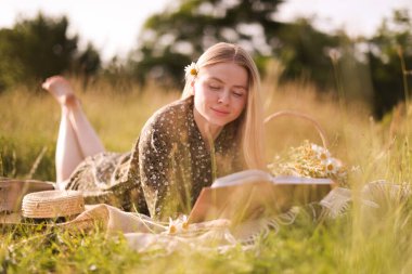 Bir buket kır çiçeğiyle çayırda kitap okuyan güzel bir kadın.