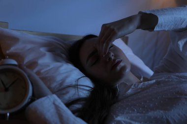 Evde yatağında uykusuzluk çeken, çalar saati olan hayal kırıklığına uğramış bir kadın.