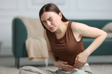 Karın ağrısı çeken bir kadın evinde yerde yatıyor, mesaj için yer var.