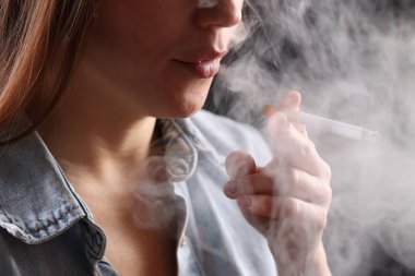 Arka planda sigara içen tişörtlü bir kadın, yakın plan. Kötü alışkanlık.