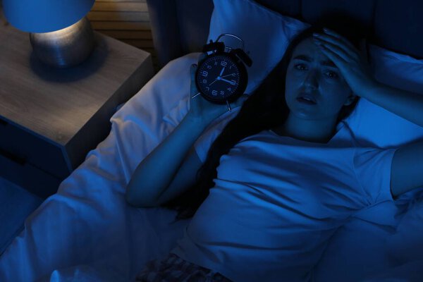 Разочарованная женщина с будильником страдает от бессонницы в постели дома, над видом