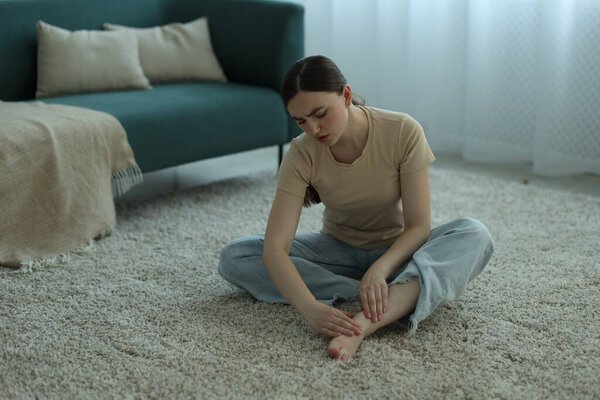 Woman suffering from foot pain on floor at home