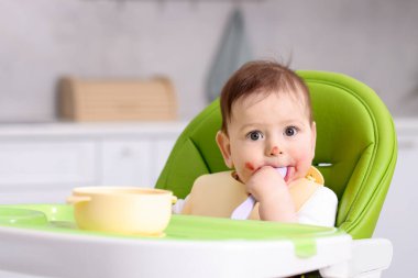 Evdeki beslenme sandalyesinde yemek yiyen şirin bir bebek. Metin için boşluk