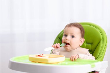 Evdeki beslenme sandalyesinde yemek yiyen şirin bir bebek. Metin için boşluk