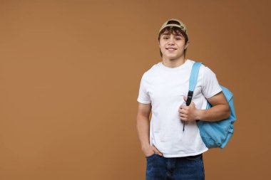 Kahverengi arka planda sırt çantası olan genç bir çocuk. Metin için boşluk