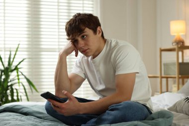Gençlik sorunları. Evde akıllı telefonlu üzgün bir genç çocuk.
