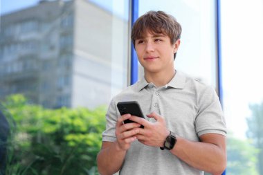 Açık hava binasının yakınında akıllı telefonu olan sevimli bir genç çocuk.