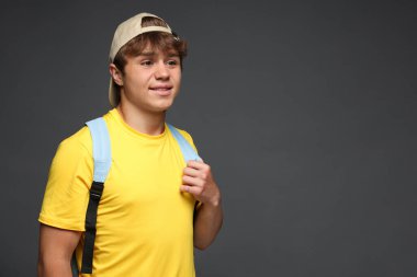 Beyzbol şapkalı, gri arka planda sırt çantalı gülümseyen genç çocuk. Metin için boşluk