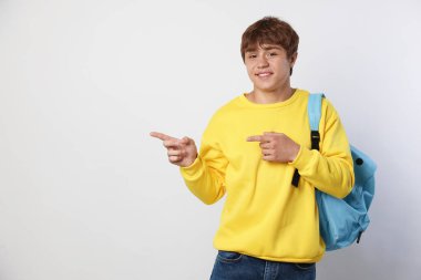 Sırt çantalı gülümseyen genç çocuk açık gri arka planda bir şeyi işaret ediyor. Metin için boşluk