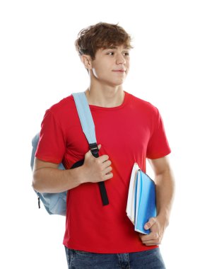 Sırt çantası ve beyaz arka planda defterleri olan mutlu genç çocuk.