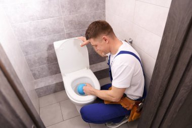 Tesisatçı içeride pompayla tuvaletin tıkanmasını açıyor.