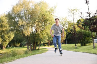 Genç adam yaz günü parkta paten kayıyor.