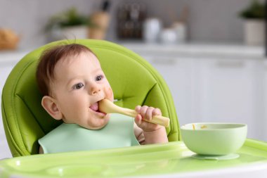 Evdeki beslenme sandalyesinde yemek yiyen şirin bir bebek.