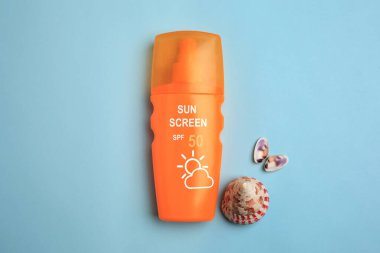 Güneş kremi ve pastel mavi arka planda deniz kabukları, üst manzara. Güneş koruma ürünü