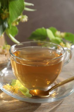 Lezzetli ıhlamur çayı fincanda, kaşıkta, yapraklarda ve çiçeklerde ahşap masada gri arka planda, yakın planda.