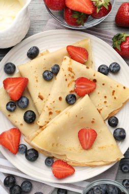 Böğürtlenli ve kremalı leziz krepler gri ahşap masada, düz yerde