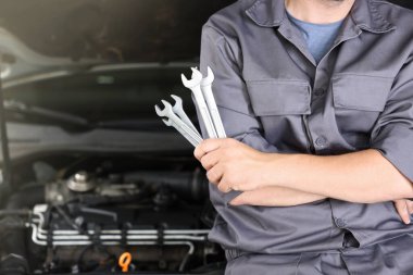 Otomobil parçaları. Kaputu açık, kapalı kaputun yanında anahtarı olan profesyonel bir tamirci, yakın plan. Metin için boşluk