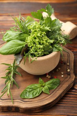 Kabuklu havan, farklı aromatik otlar ve baharatlar ahşap masada, yakın plan.