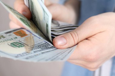 Açık gri arka planda dolar banknotları sayan kadın, yakın plan