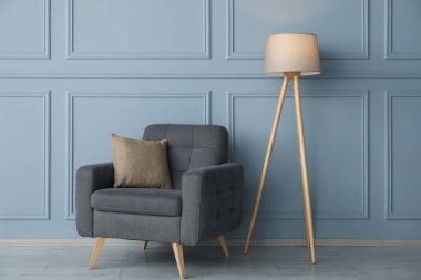 Açık mavi duvarın yanında rahat bir koltuk ve lamba.