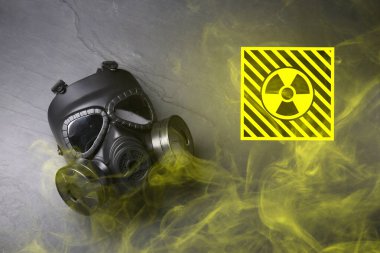 Radyasyon tehdidi. Gaz maskesi, radyoaktif tabela ve gri arka planda duman, üst görünüm